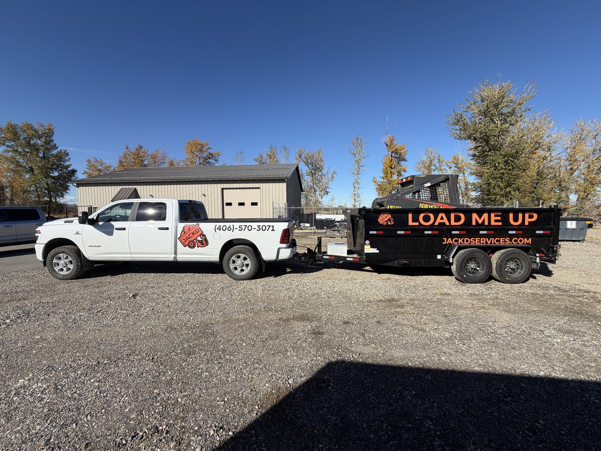 Skid steer sitting in the JACKD dump trailer behind the Ram